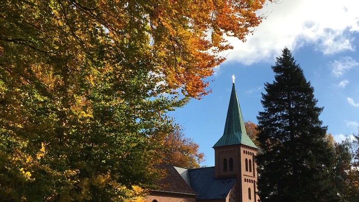 En kirke med spir med høstfarvede træer og blå himmel