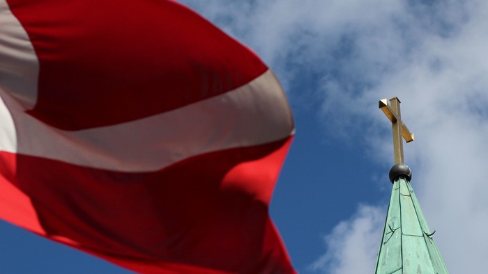 En rød hvid flag ved siden af en grøn kirke spire med kors.