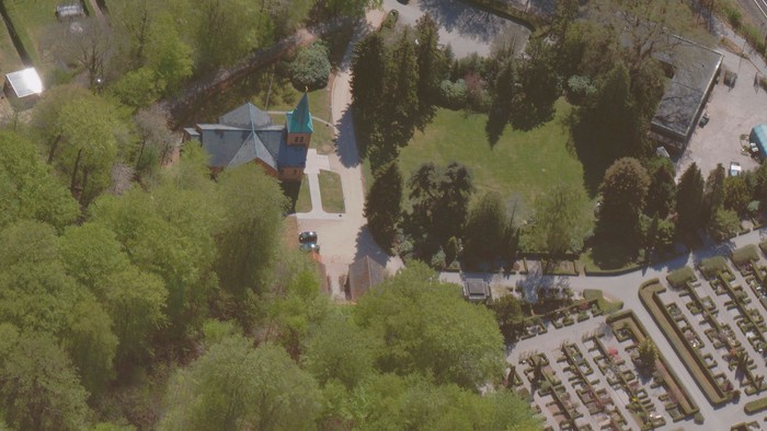 Luftfoto af en frodig park med et farverigt pavillon, omgivet af bolighuse og kirkegårdsarealer.