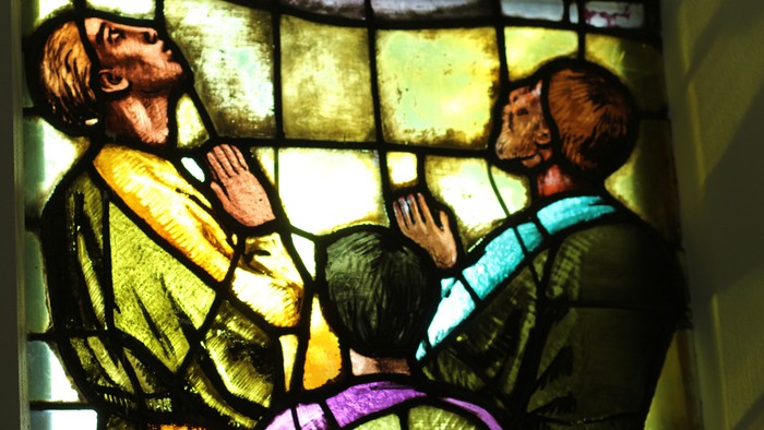 Farvet glasbillede, der forestiller en skægget figur, som velsigner et knælende barn, med levende farver og detaljeret design.