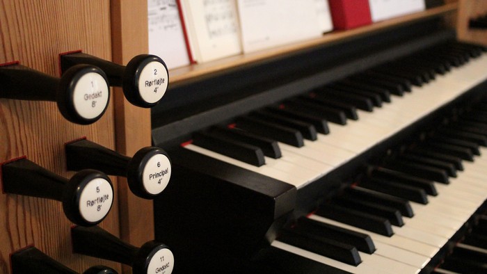 Nærbillede af et orgelkonsol med manualtaster og mærkede registre til musikalsk styring.
