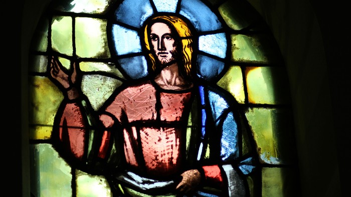 Farvet glasafbildning af Jesus Kristus med et roligt udtryk og åbne hænder.