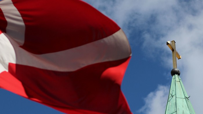 En rød hvid flag ved siden af en grøn kirke spire med kors.