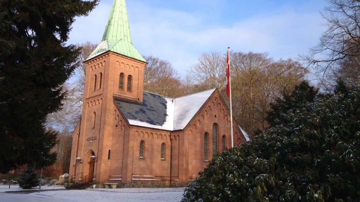 En rød murstenskirke med grøn spire og flagstang.