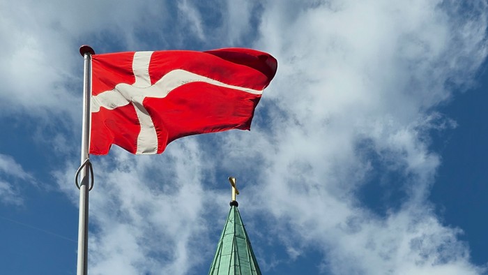 Dansk flag vimpler i blå himmel med hvid skygge.