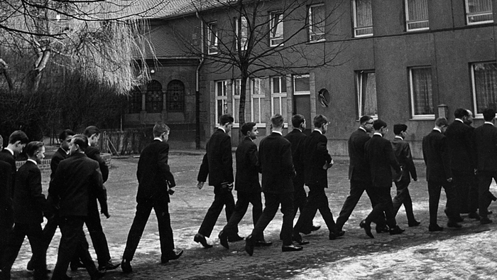Eine Gruppe von Menschen geht an einer großen, historischen Steinkirche mit hohen Türmen und gewölbten Fenstern vorbei.