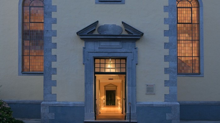 Eleganter Gebäudeeingang mit gewölbten Fenstern, die in der Dämmerung warm leuchten, gerahmt von klassischer Steinarchitektur.