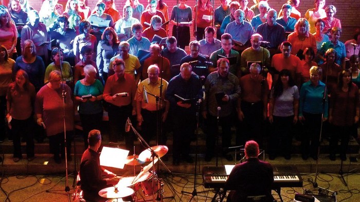 Große Gruppe von Musikern und Sänger auf Bühne, verschiedene Instrumente, darunter Gitarren und Tasteninstrumente