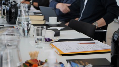 Professionel mødeopsætning med dokumenter, vandglas og snacks på et konferencebord.