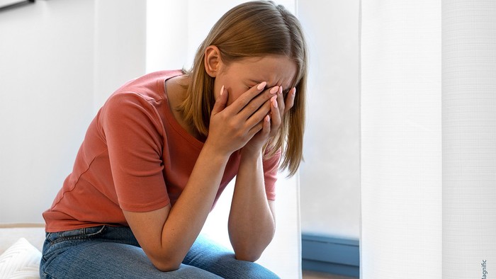 Eine Person, die mit dem Gesicht in den Händen dasitzt und verzweifelt oder aufgebracht wirkt, drinnen.