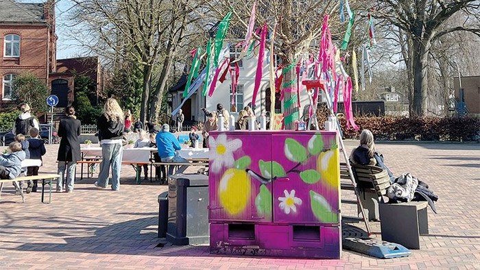 Bunte Freiluft-Kunstinstallation mit bemalten Kisten und festlichen Dekorationen auf einem öffentlichen Platz.