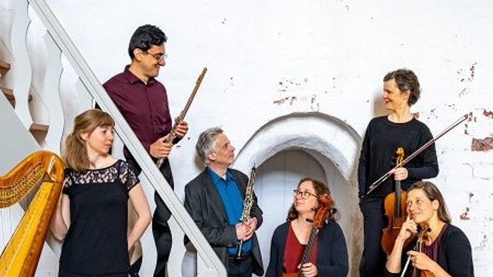 Ein Ensemble von Musikern posiert mit ihren Instrumenten in einem historischen Raum