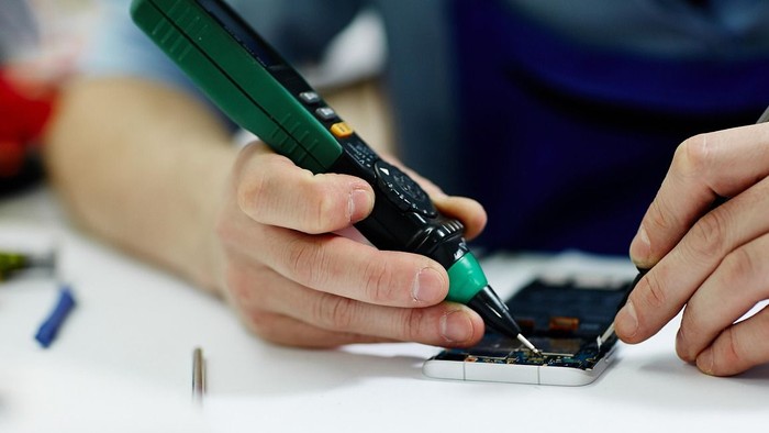 Eine Person repariert ein elektronisches Gerät mit einem Schraubendreher und Zange.