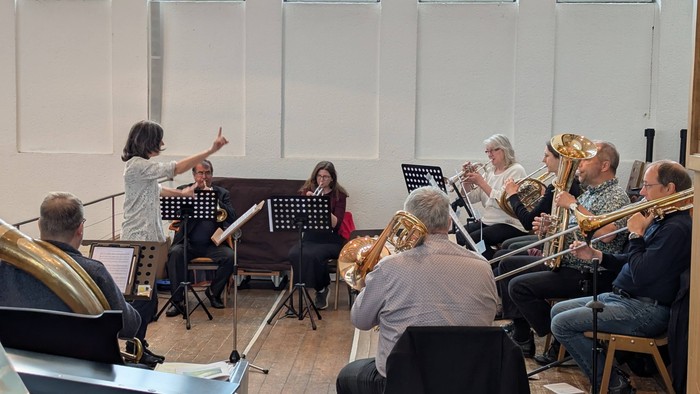 Ein Orchester probt unter Leitung einer Frau in einem hellen Raum