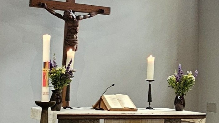 Ein Kirchenaltar mit Kreuz und Kerzen vor einem bunten Fenster
