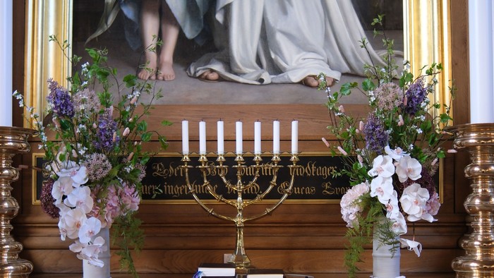 Elegant alter med religiøs kunst, blomsterdekorationer og en lysestage på træpanelering.