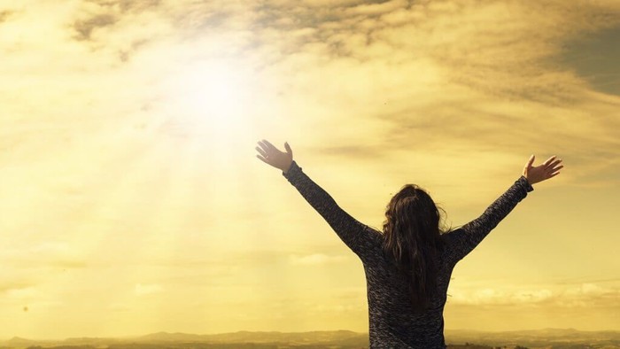 A person stands with arms raised against a backdrop of a cloudy, golden sky.