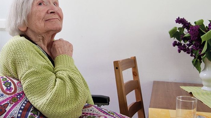 Alte Frau sitzt in einem Stuhl und schaut zur Seite