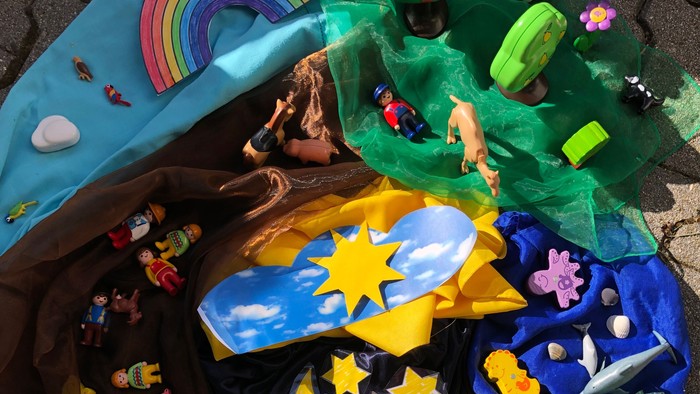 Kindergottesdienst Beispielbild, bunte Tücher auf Steinboden, mit Regenbogen, Tiere und Pflanzen dekoriert