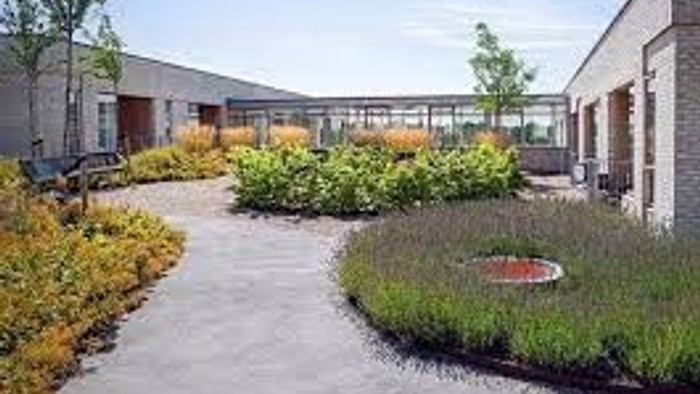 En smuk have med blomster og en lille springvand i forgrunden og et hus i baggrunden