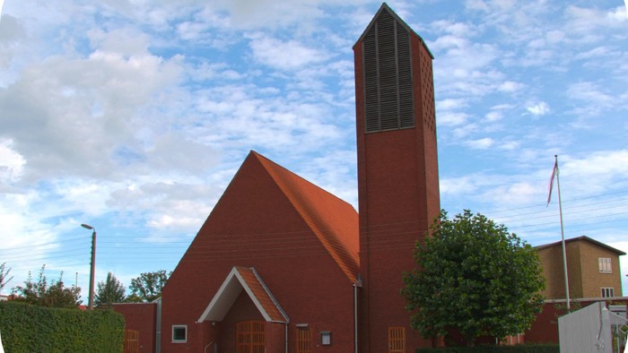 Rødt kirke med høj tårn og grønne buske foran