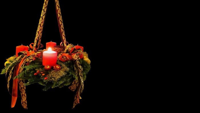 Ein Adventskranz mit brennender Kerze hängt an einem dunklen Hintergrund
