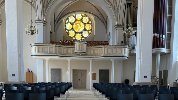 In der Kirche steht ein Blumenarrangement vor dem Altar, umgeben von Stühlen.