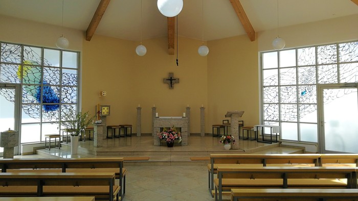 Leere Kirche mit Holzbänken und großen Fenstern