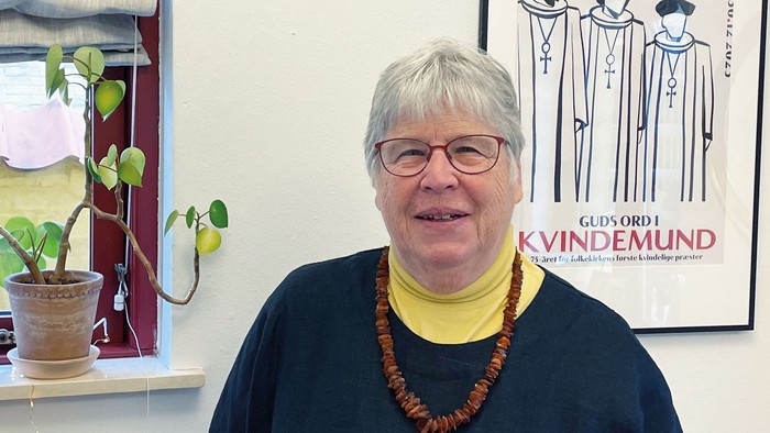 En kvinde står i et rum med en plante og en plakat på væggen.