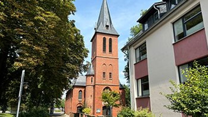 Ein rotes Backsteingebäude mit einem hohen Turm steht neben einem modernen Gebäude.