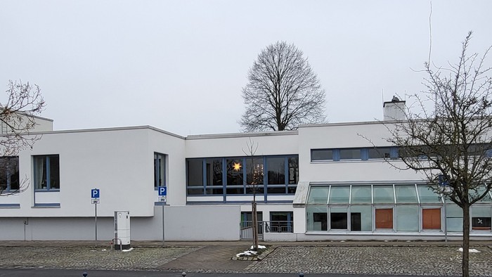 Modernes Gebäude mit großen Fenstern und Bäumen davor.