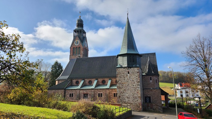 Altes Steinhaus mit hohem Turm und spitzem Dach, umgeben von Grün und Bäumen