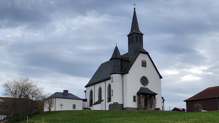 Weiße Kirche mit hohem Turm auf grünem Hügel.