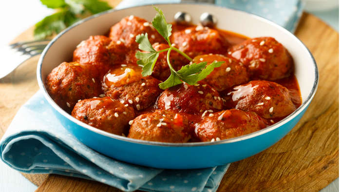 En blå bowl med rødt stegt kød og grønne urter på et træbord.