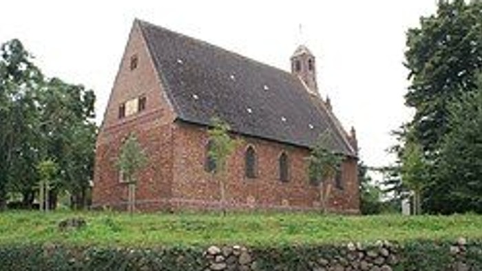 Historische Backsteinkirche mit steilem Dach und Glockenturm in einer üppigen, grünen Landschaft.