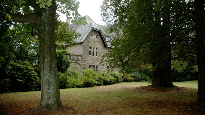 Ein großes, altes Haus umgeben von Bäumen und Grün.