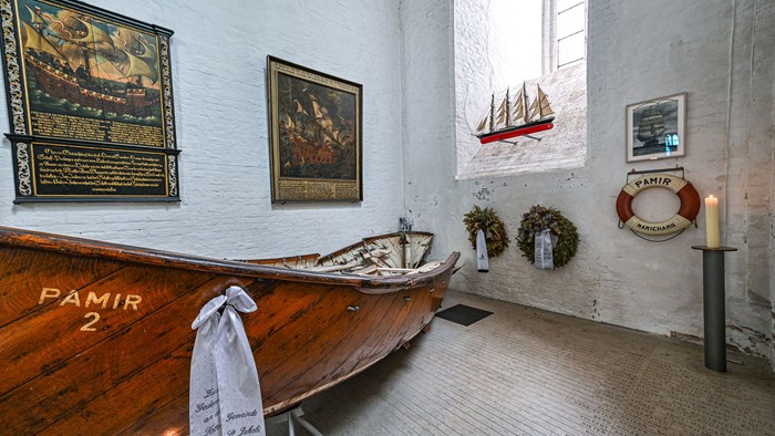 Historisches Schiffsmodell und maritime Artefakte in einem weiß gestrichenen Raum mit einem hölzernen Boot namens *Pamir* ausgestellt.