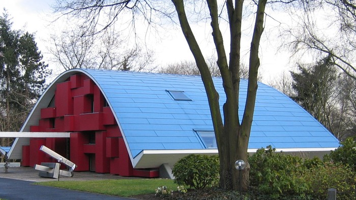 Ein rotes und blaues Gebäude mit einem gewölbten Dach neben einem Baum.