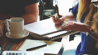 En gruppe af mennesker sidder ved et bord med laptopter, noter og kaffe.