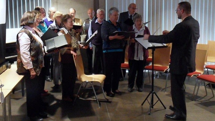 Ein Mann leitet einen Chor, der Noten liest