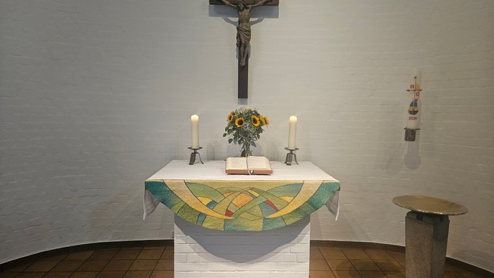 Ein Altar mit Kreuz, Kerzen und Blumen in einem Kirchenraum