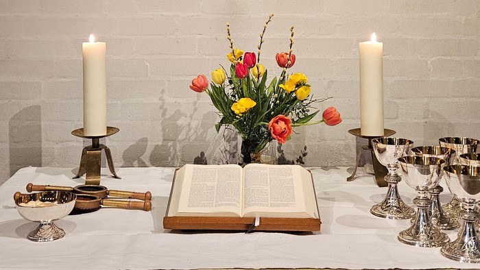 Ein Tisch mit Kerzen, Blumen und einem Buch vor einer Ziegelwand