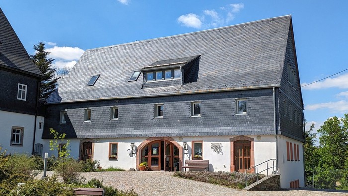 Zweistöckiges Haus mit grauer Schieferfassade und Holzfenster, umgeben von grünem Garten