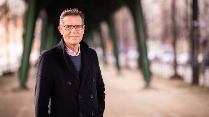 Mann mit Brille und dunklem Mantel steht in einem Park.
