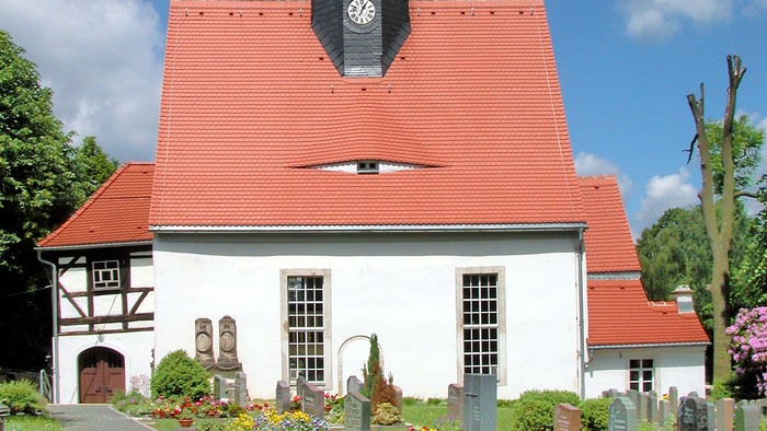 Kleine weiße Kirche mit rotem Dach und schwarzem Turm.