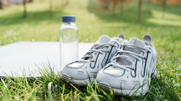 Ein Paar graue Turnschuhe und eine Wasserflasche auf einem grasbewachsenen Weg