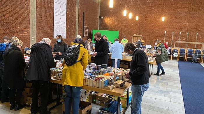 Menschen bei einem Buchmarkt in einem Raum mit Backsteinwänden