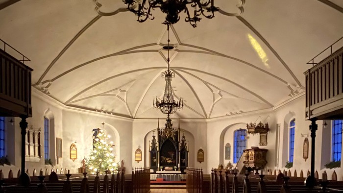 Indre del af kirke med høje vægge og hængende lygter.