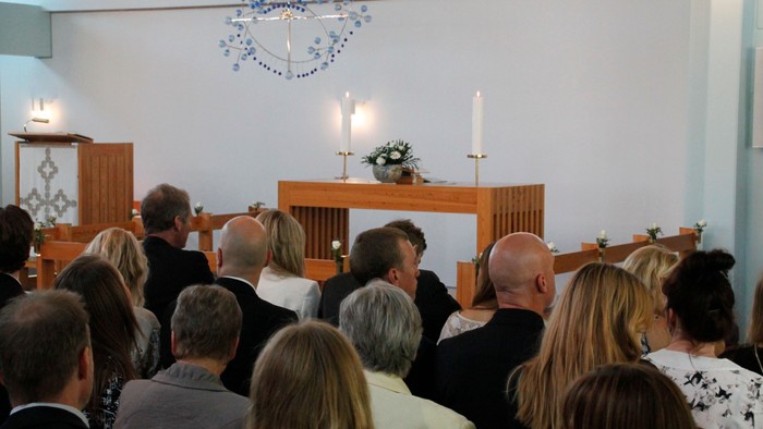 En kirkeindendring med forsamling og alter med lysstake og blomster.