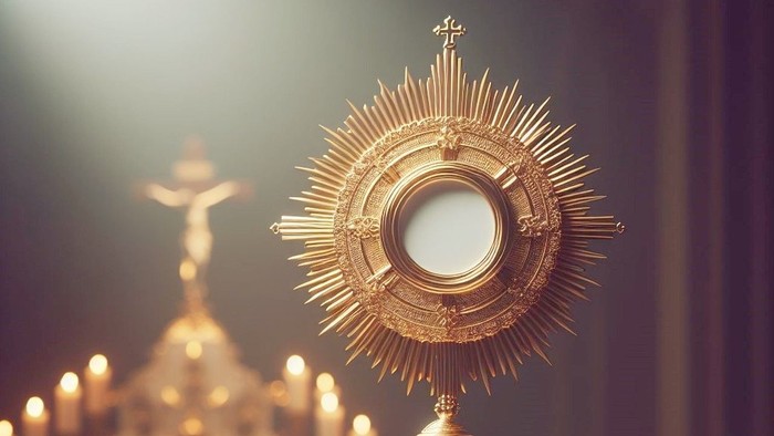 Goldene Monstranz auf einem Tisch mit brennenden Kerzen und einem Kruzifix im Hintergrund.